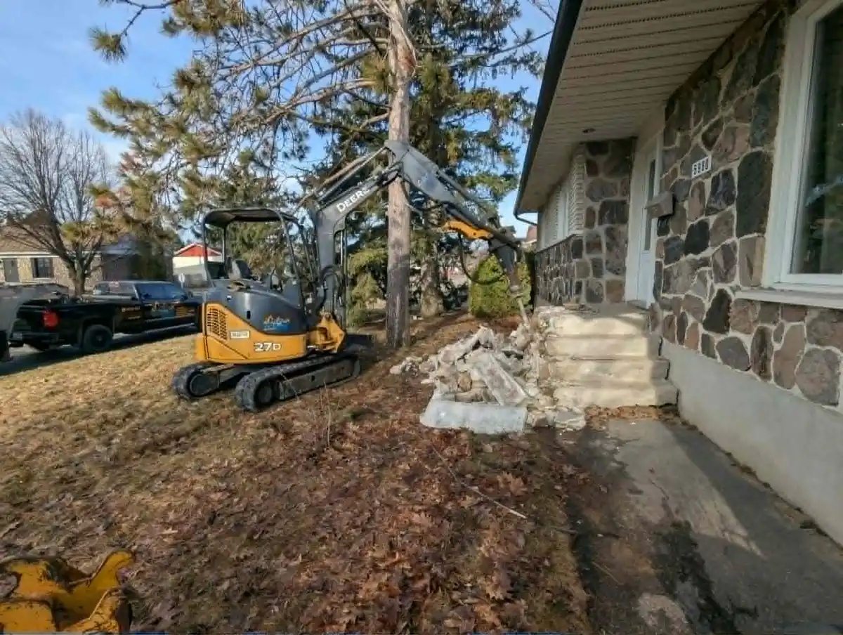 Mini-excavatrice effectuant la démolition d’un escalier en béton devant une résidence